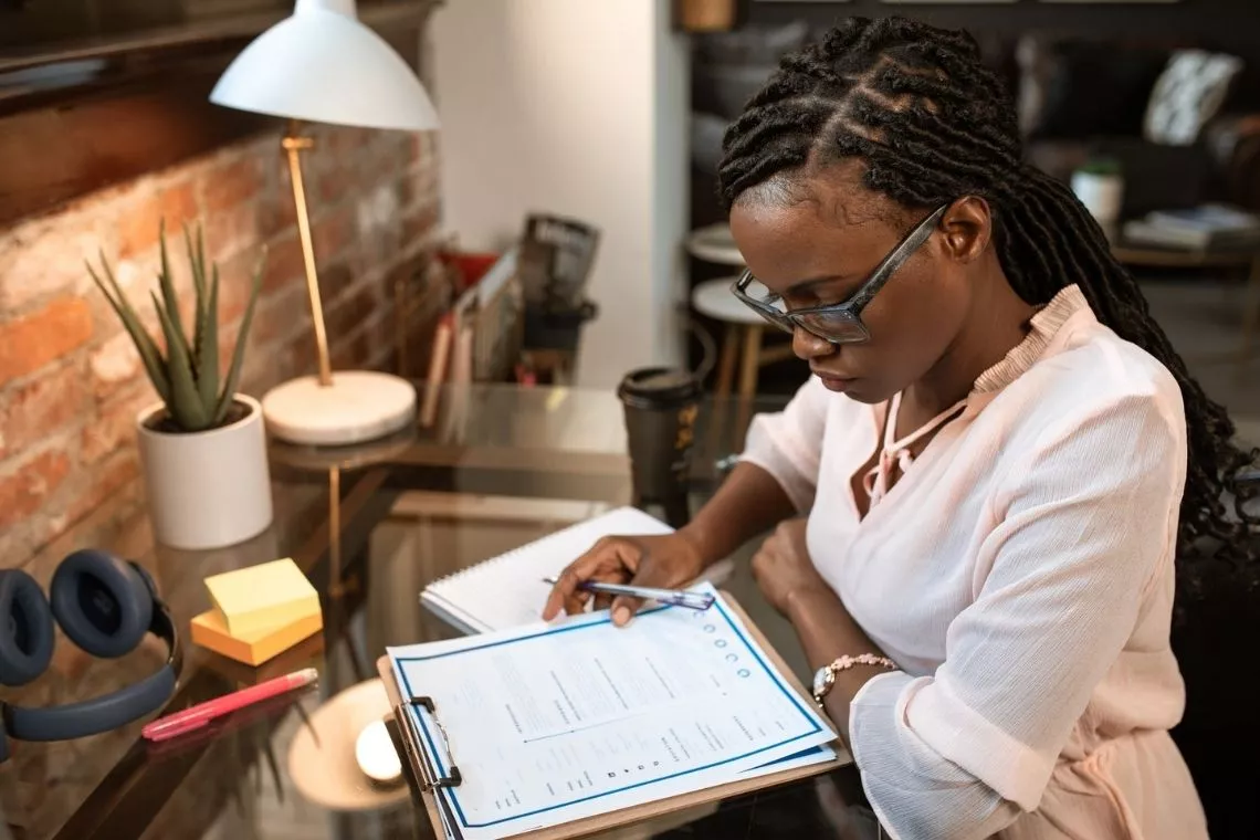 A professional writing a personalized cover letter on a laptop next to a coffee cup on a clean wooden desk